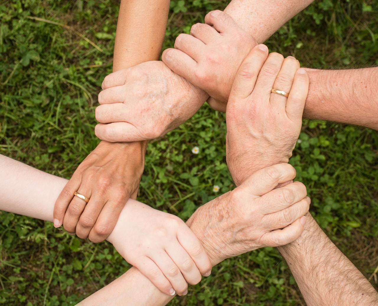 Services-02 Close-up of diverse hands forming a connection, symbolizing teamwork and unity outdoors.